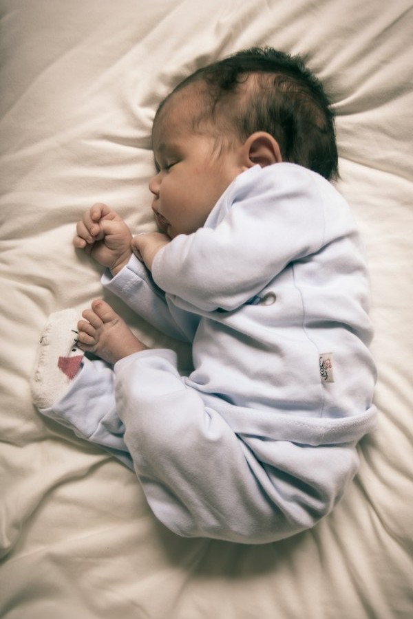 Un bébé qui dort paisiblement, blotti sur le côté, en pyjama bleu clair